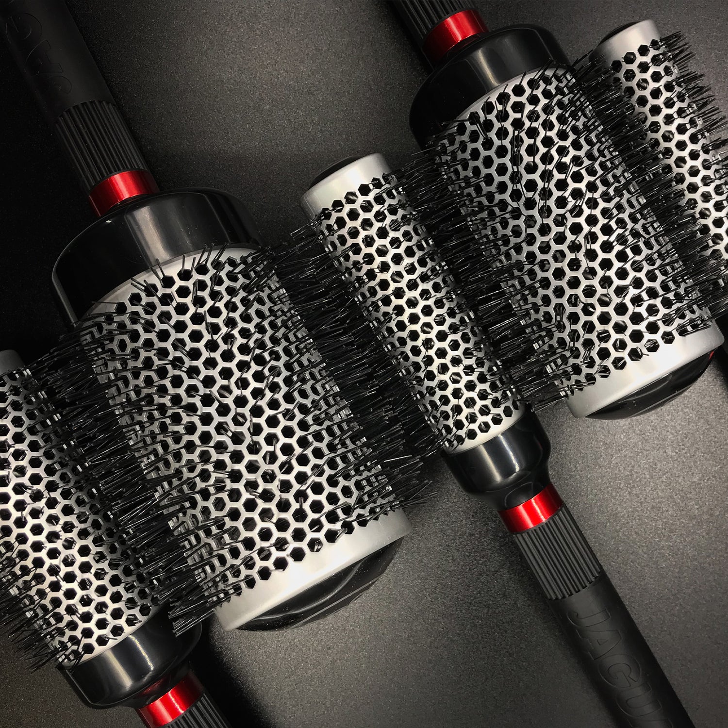JAGUAR T-series round brushes in various sizes with honeycomb body and heat-resistant bristles, close-up on dark background.