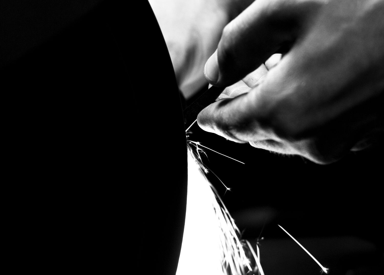Close-up in black and white: a hand carefully sharpens hairdressing scissors on a whetstone at the JAGUAR factory.