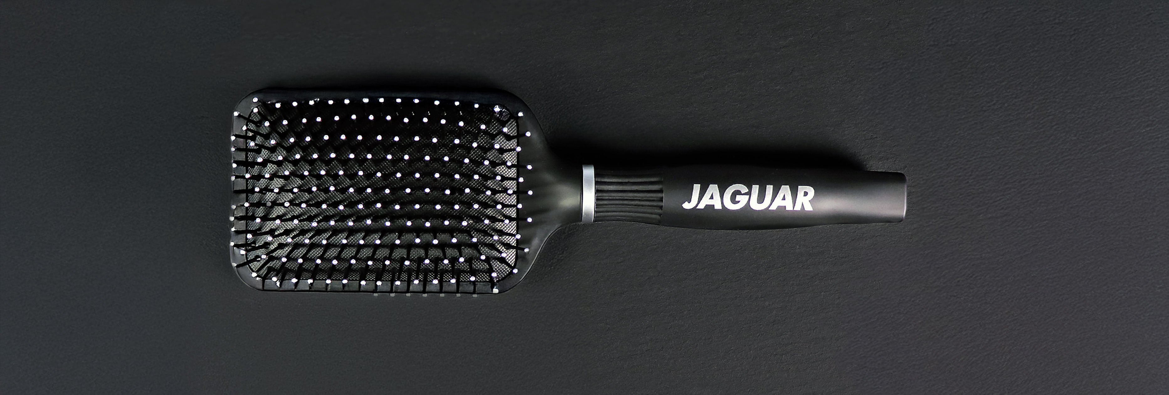 AGUAR Paddle Brush in black with nubby bristles on a dark background.
