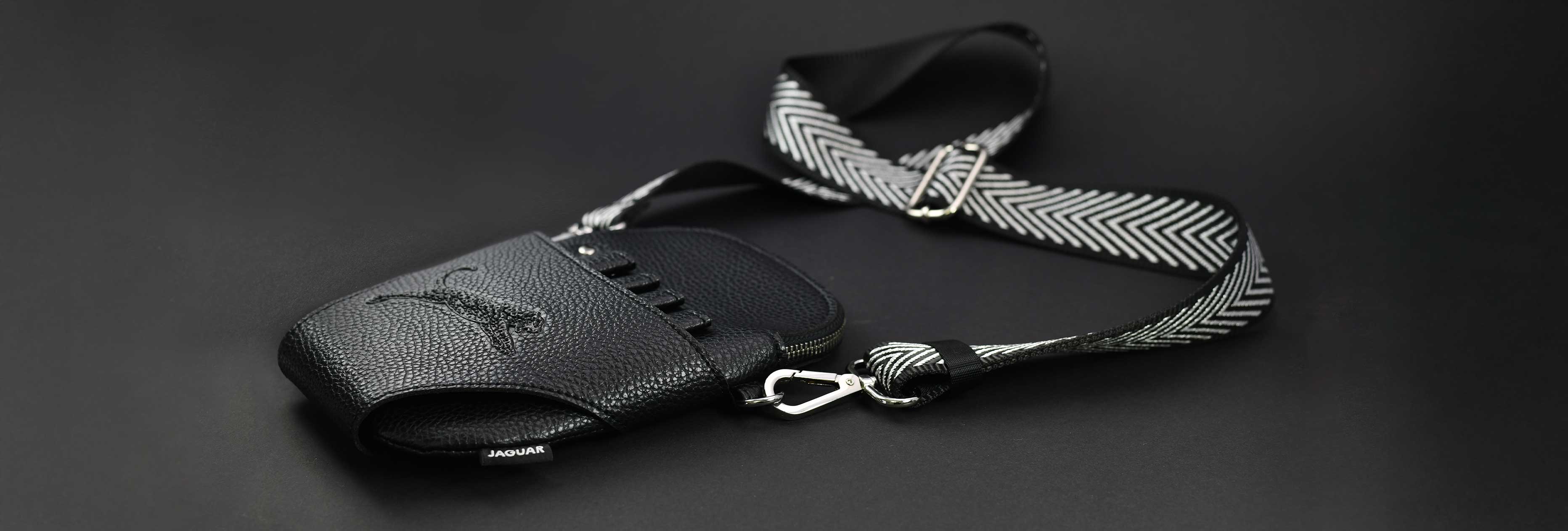 Black JAGUAR leather hairdresser's holster with adjustable black and white shoulder strap on a dark background