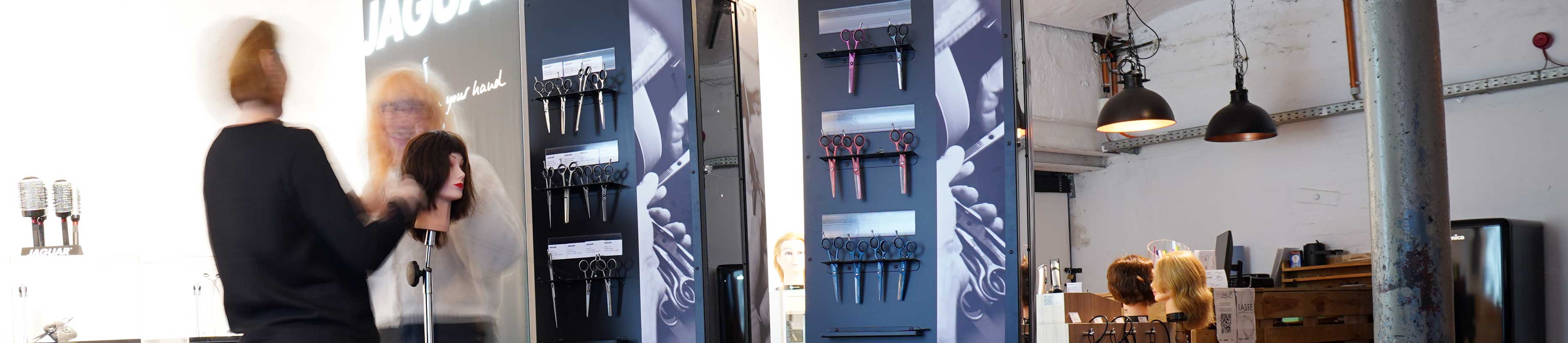 JAGUAR Store directly at the factory in Solingen: View of the showroom with hairdressing scissors on display, training heads, and consultation situation in an industrial workshop atmosphere.